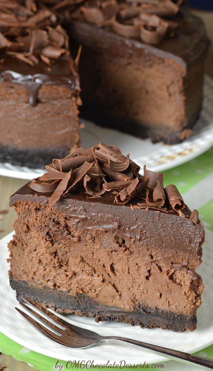 Decadent piece od Triple Chocolate Cheesecake on a whit plate with a whole cake behind.