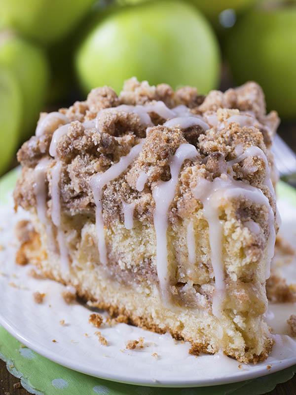 Piece of Cinnamon Apple Crumb Cake in front of bunch of apple.