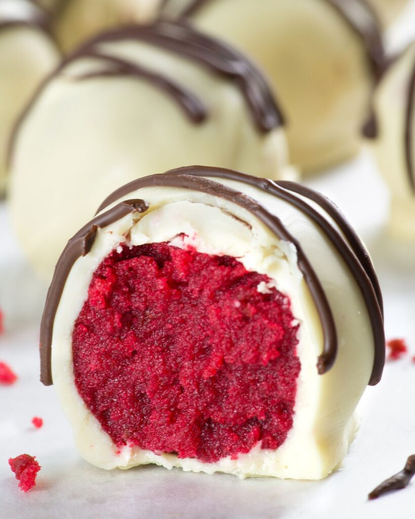 Red velvet truffle cut in half to show its bright red, creamy center, coated in white chocolate and drizzled with dark chocolate.
