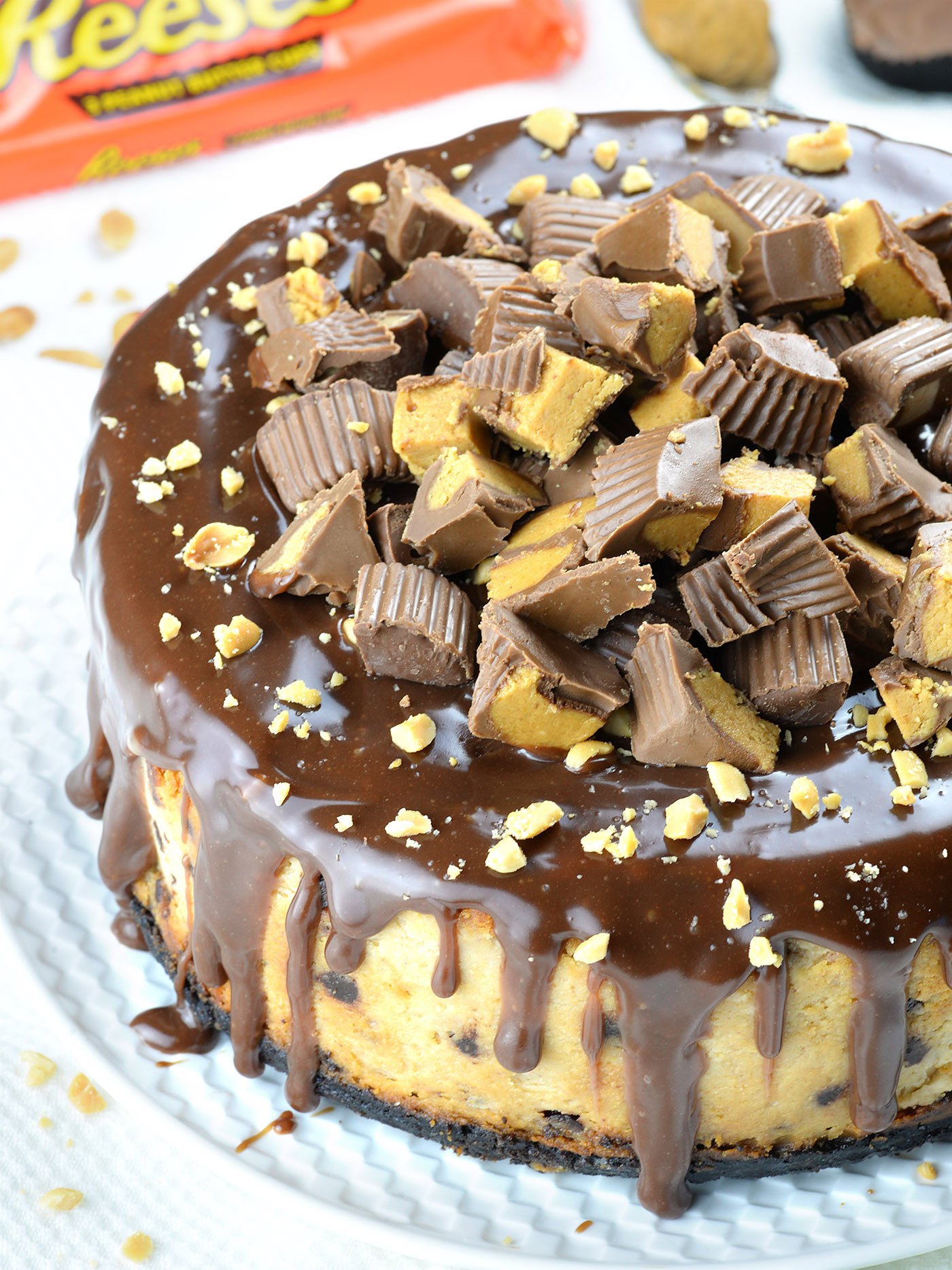 Whole chocolate peanut butter cheesecake topped with chopped peanut butter cups and drizzled chocolate ganache.