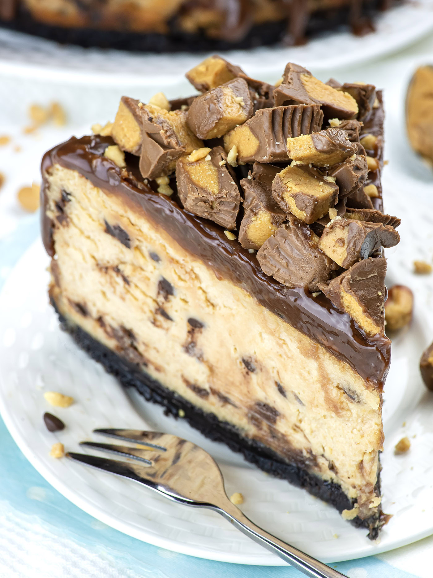 A rich slice of chocolate peanut butter cheesecake topped with chopped peanut butter cups on an Oreo crust.