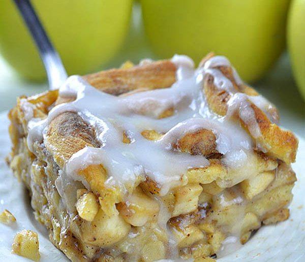 Piece of Caramel Apple Cinnamon Roll Lasagna on a white plate in front of bunch of apples.