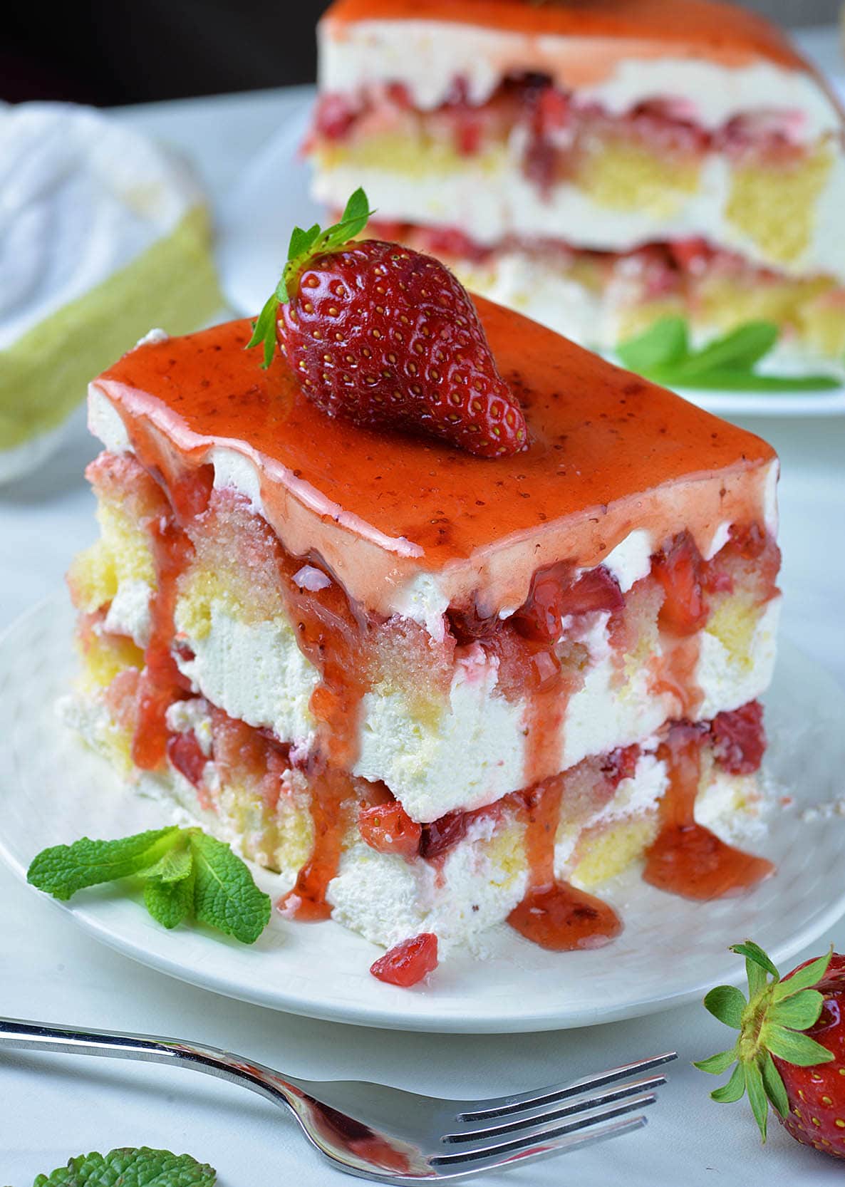 Piece of frozen strawberry shortcake dessert on white plate garnished with strawberry on top.