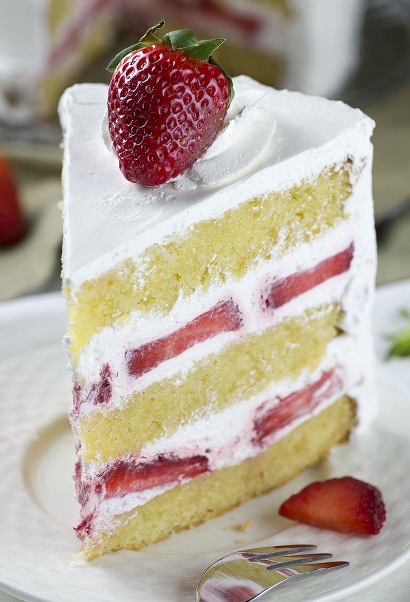 Piece of strawberry shortcake cake on a plate with garnished strawberries.