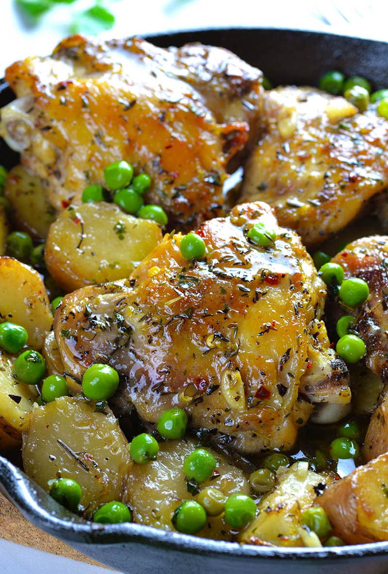 Big chicken breast in a pan full with baked potatoes and beas.