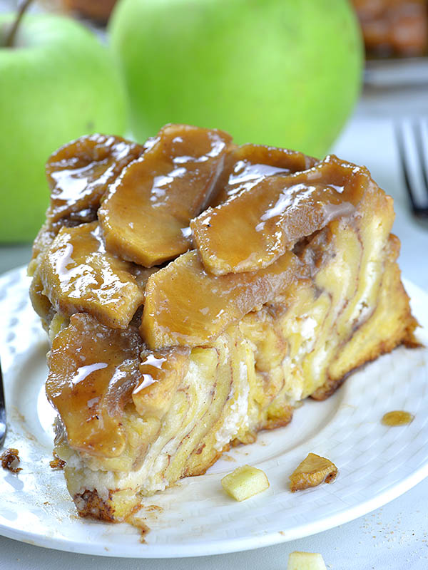 Piece of Upside Down Apple Cinnamon Roll Cake on a white plate with two apples behind.