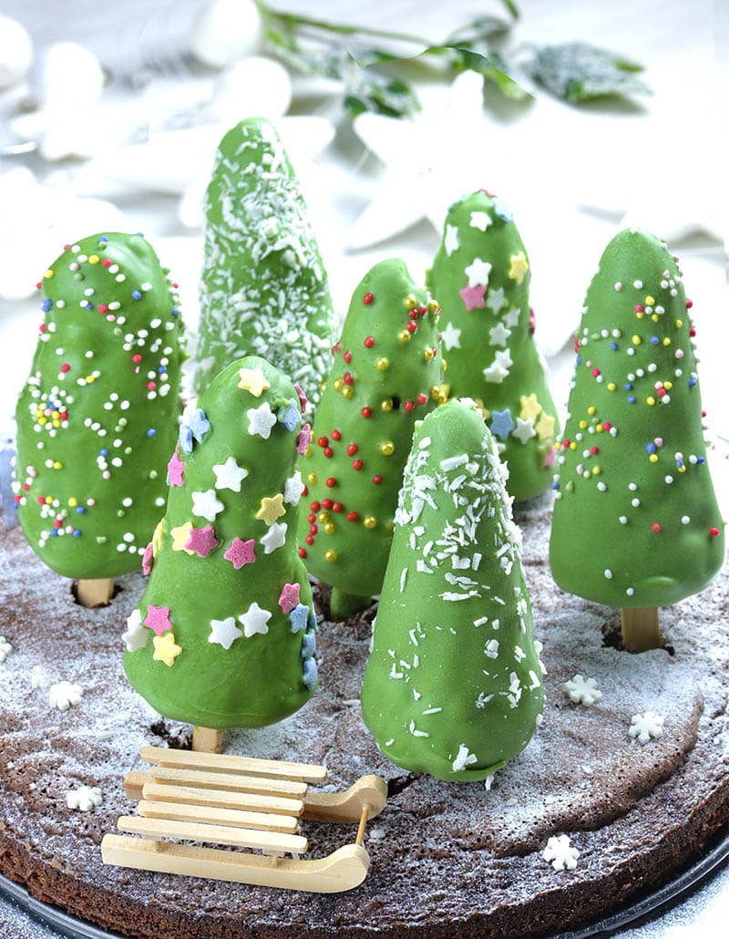 Christmas Tree Cheesecake on a stick on a chocolate cake in form of snow forest. 