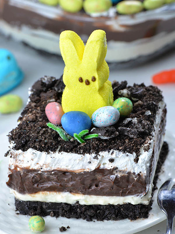 Four layered Easter Chocolate Lasagna garnished with Oreo dirt on top, Peeps Bunny and couple of Easter eggs candy.