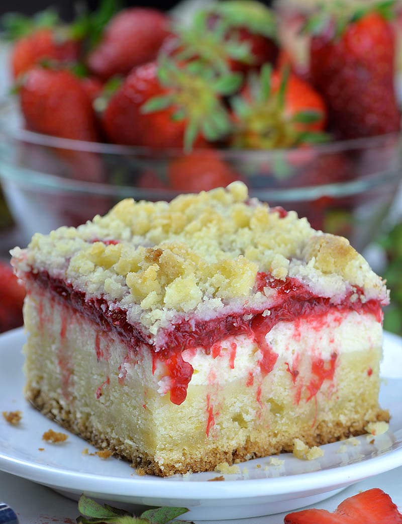 Big piece of Strawberry Coffee Cake on white plate in front of strawberry bowl.