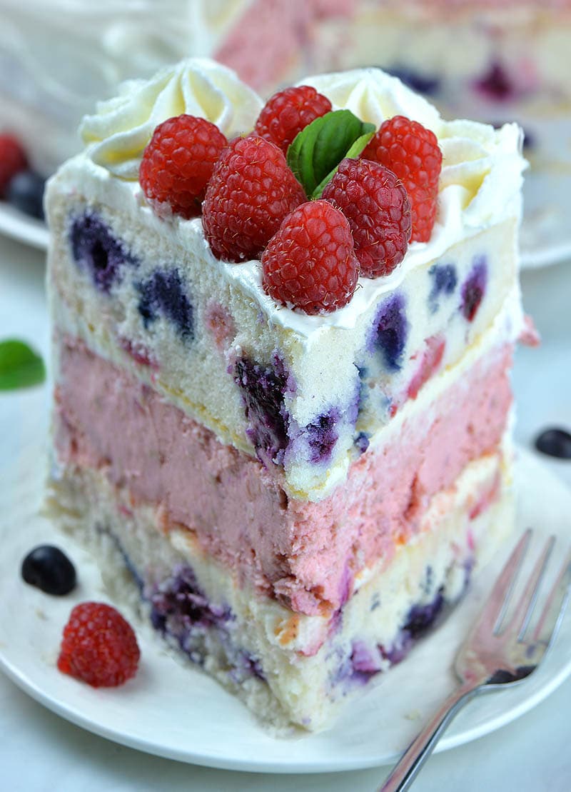 Raspberry Cheesecake Cake piece on white plate with fork and raspberry and blueberry decoration.