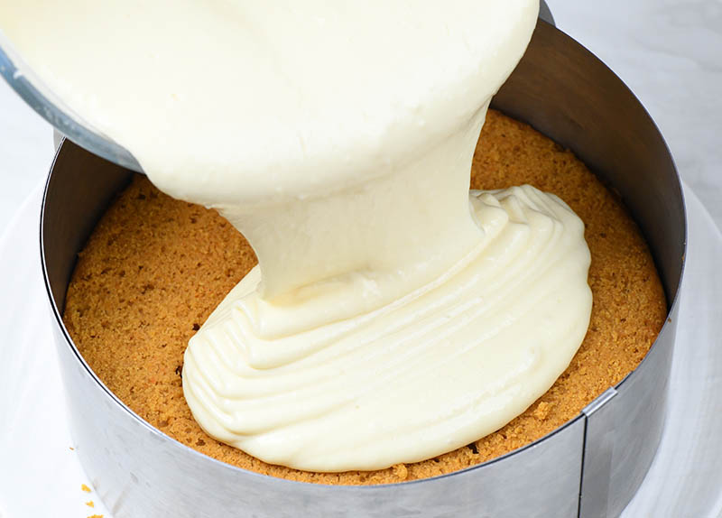Pouring cheesecake mixture over baked pumpkin bread cake.