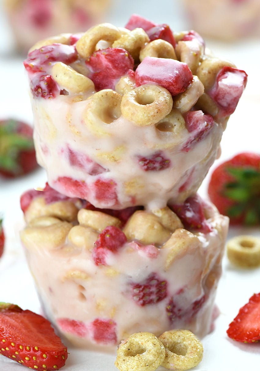 Two White Chocolate Strawberry Cheerios Cups each on other with couple of strawberries beside.