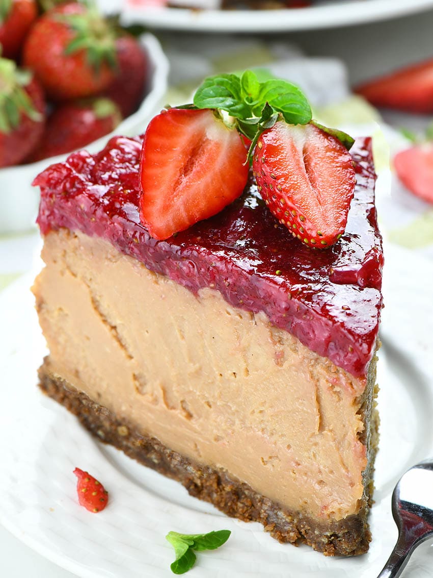 Piece of Strawberry Chocolate Cheesecake on a white pate garnished  with two half strawberries.