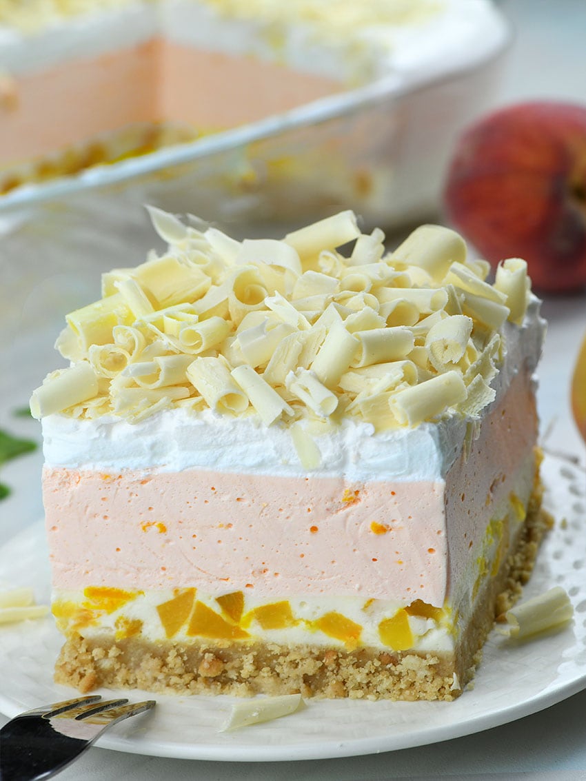 No Bake Peach Jello Lasagna on a white plate with peaches behind.