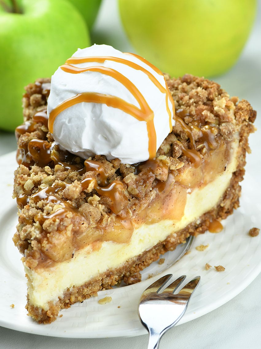 Apple Crisp Cheesecake on white plate with whipped cream ball on top and caramel topping.
