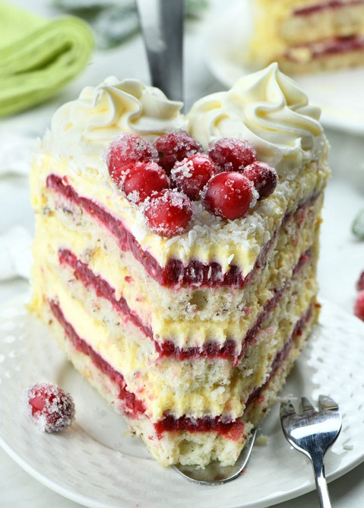 Piece of White Chocolate Cranberry Layered Cake on a white plate with cranberry decoration.