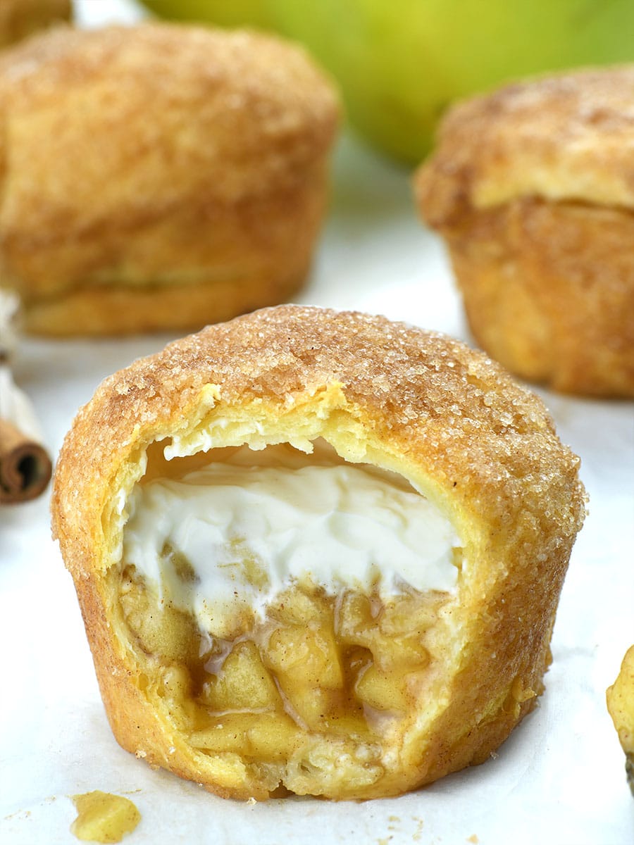 Apple Pie Crescent Muffin in front. Couloe of muffins behind and bunch of apples.