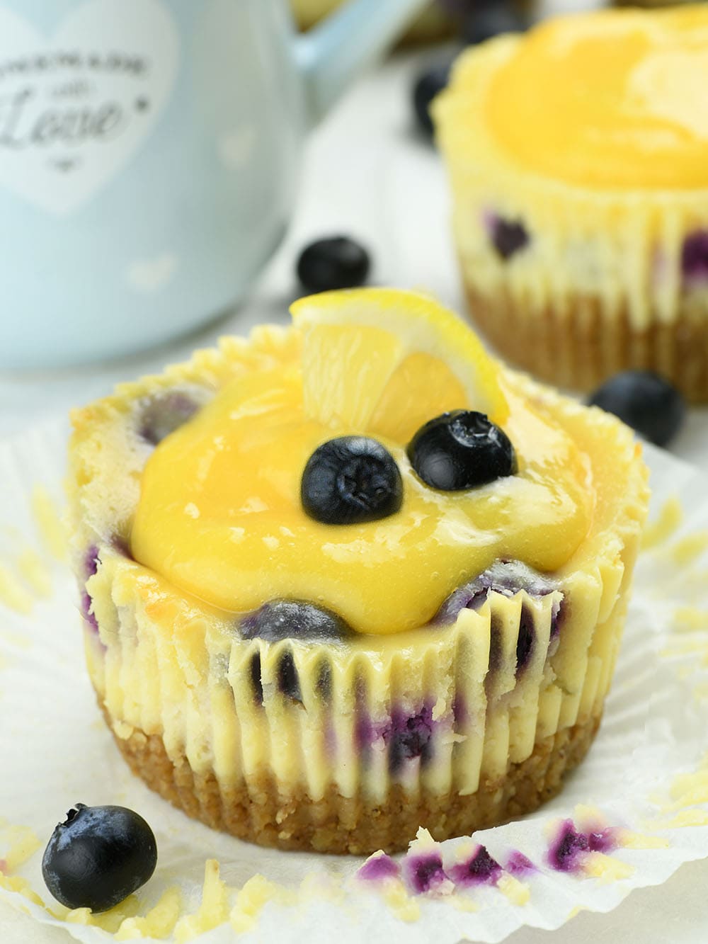 Mini Lemon Blueberry Cheesecakes with Lemon Curd and garnished with two blueberries and lemon.
