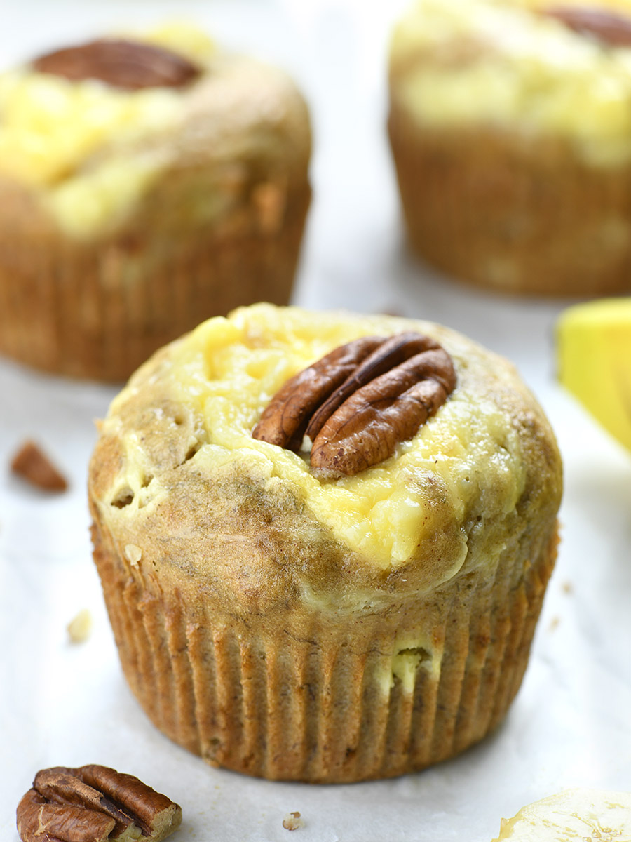 Banana Cream Cheese Muffins with pecan on the top in front of couple of  muffins.