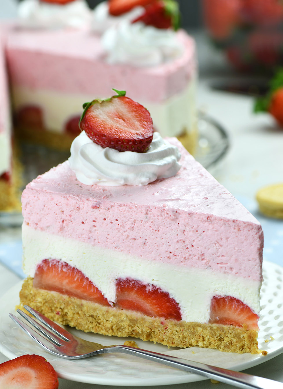 Piece of Layered No-Bake Strawberry Cheesecake on a white plate, garnished with cool whip and sliced strawberry.