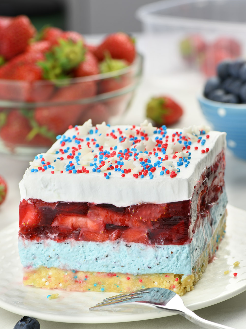 Summer Berry Jello Lasagna -  layered dessert on a white plate garnished with red and blue funffetti and white stars.
