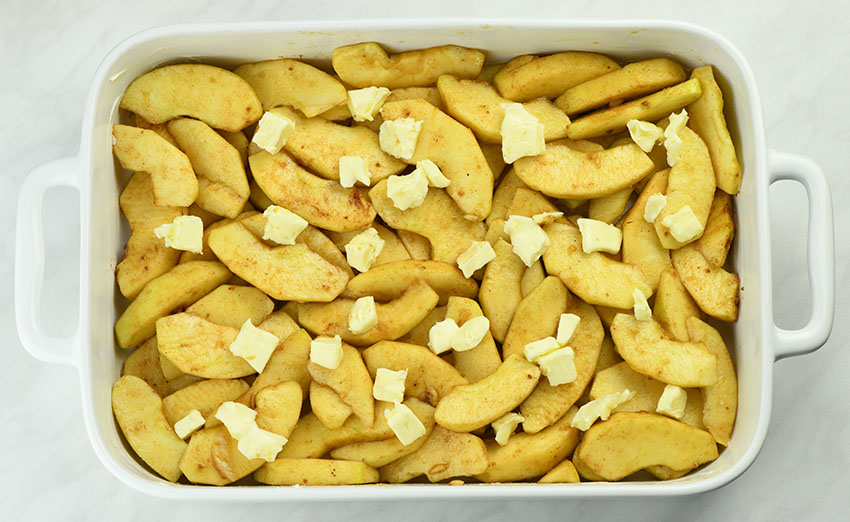 Apples arranged in a bowl and cubes of butter scattered over the apples.