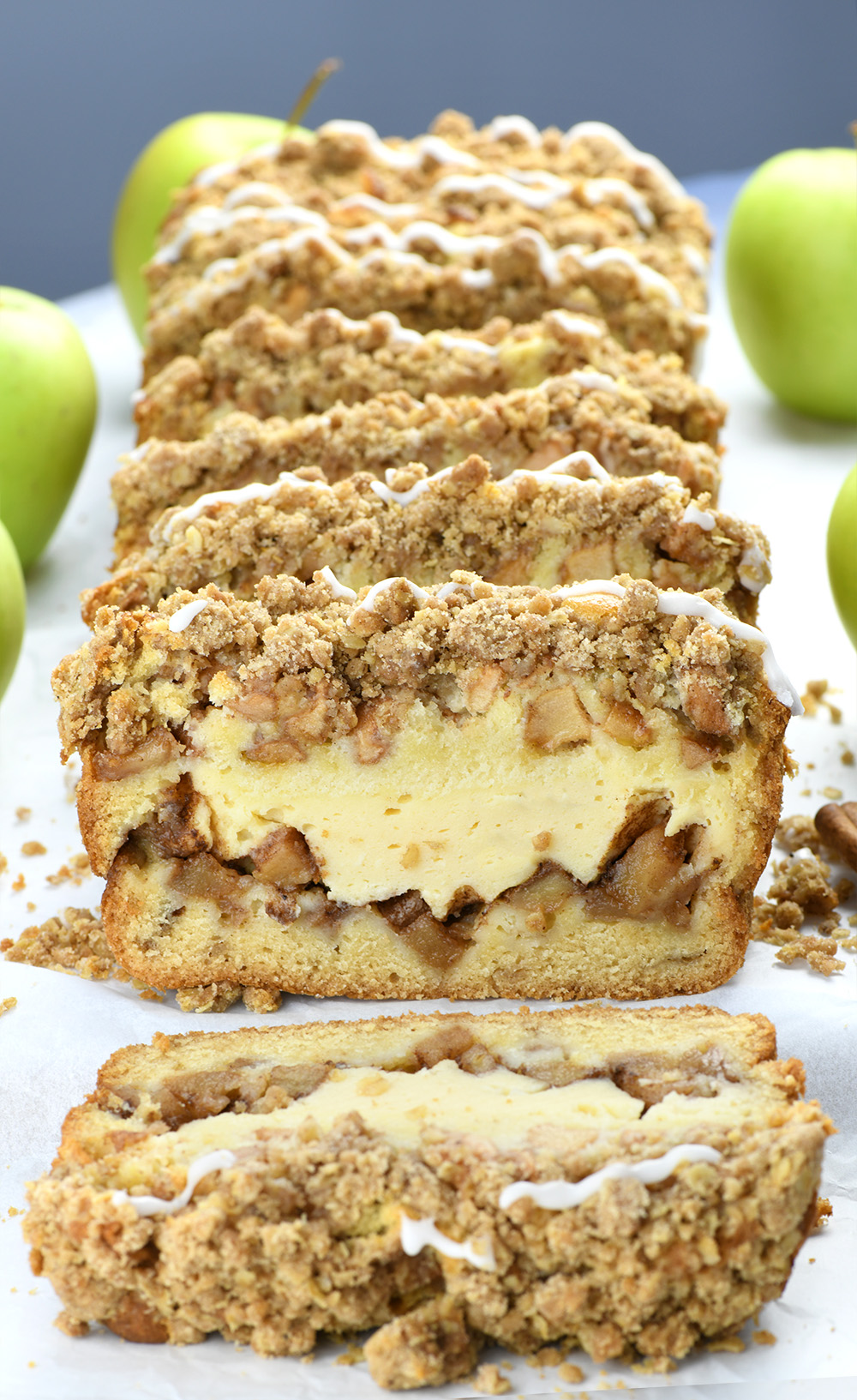 Slices of Apple Crisp Cheesecake Bread  on a white parchment paper with bunch of green apples.