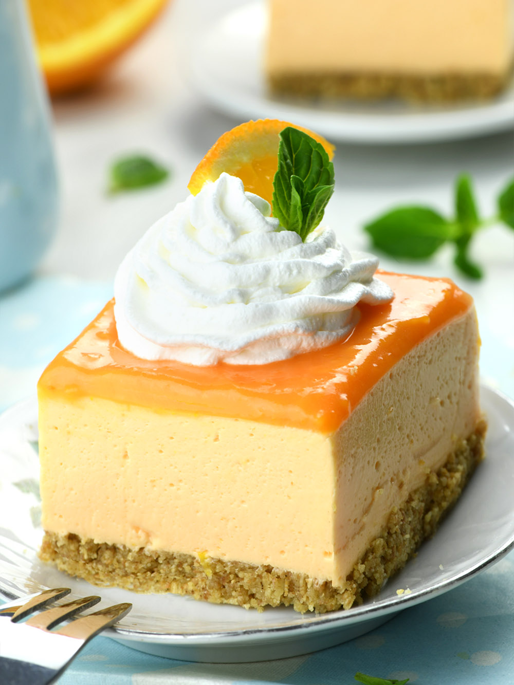 Piece of Orange Creamsicle Cheesecake Bar non a white plate, topped with whipped cream and garnished with orange slice.
