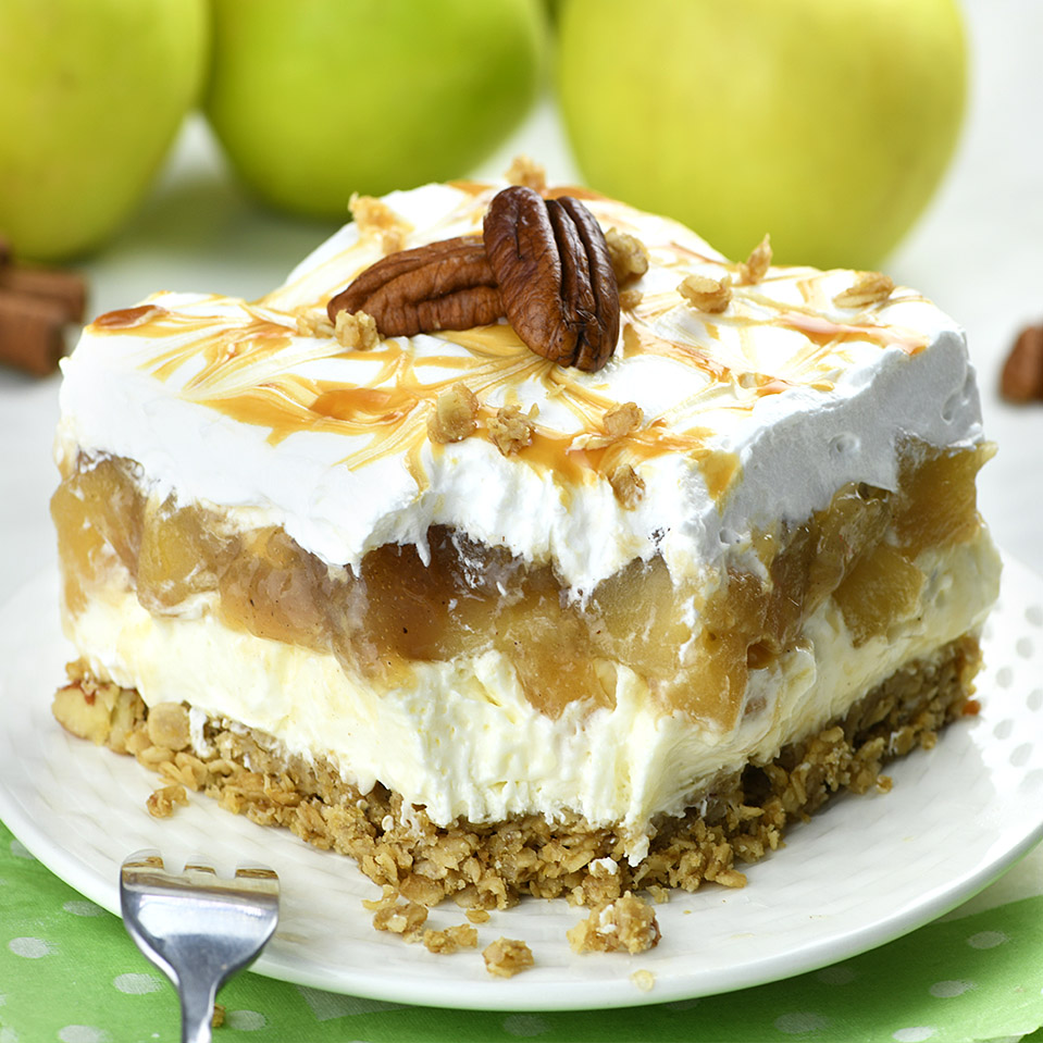 A piece of 4-layer no bake apple dessert  (oats, cheesecake, apple, whipped cream) on a plate topped with caramel.