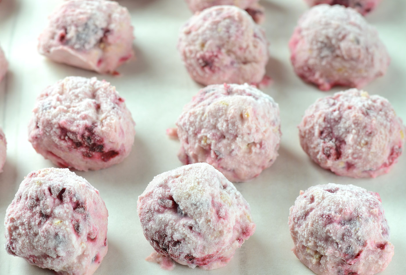 Powdery pink raspberry-flavored sugar-coated truffle balls laid out on parchment paper, in the process of chilling or setting.