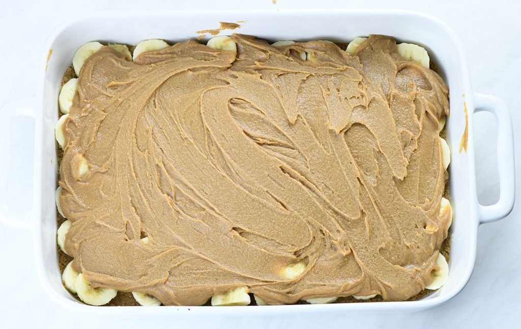 A baking dish with a layer of sliced bananas on top of a graham cracker crust, covered with a layer of smooth, spread toffee or caramel.