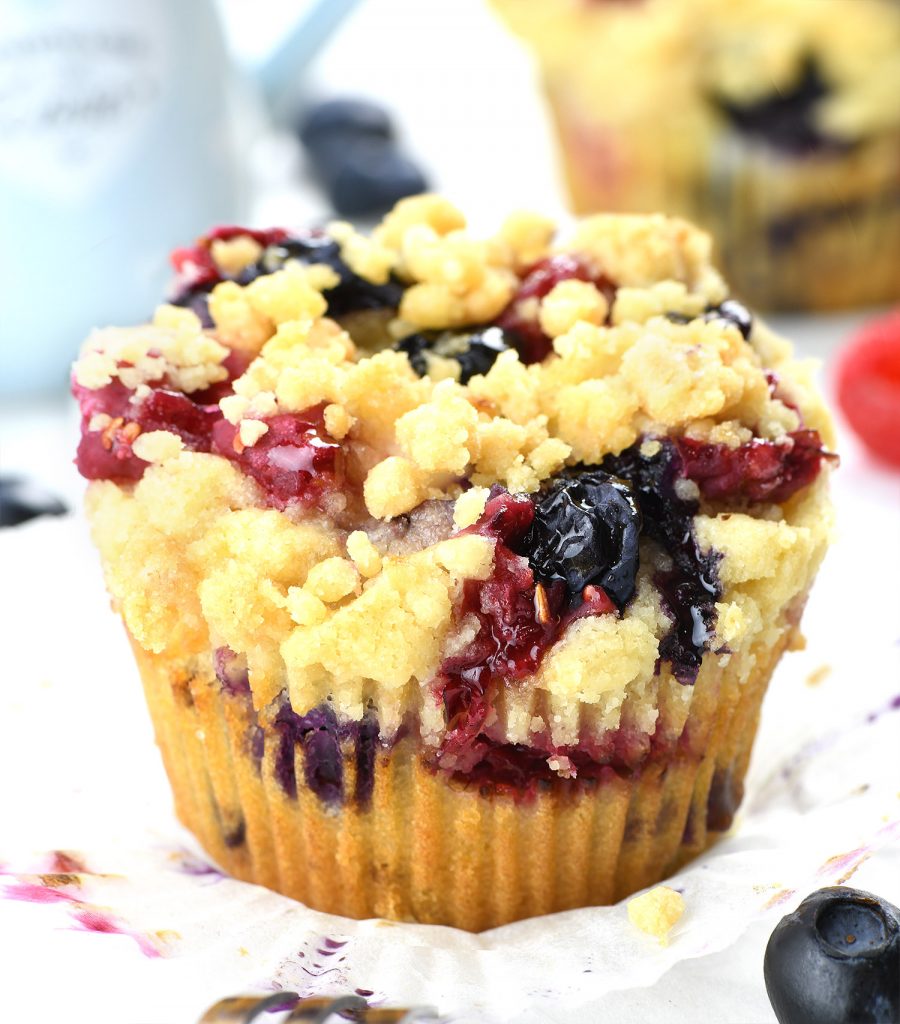 A close-up of a berry cream cheese muffin with a crumbly streusel topping, featuring blueberries and raspberries.