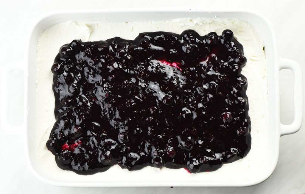 Blueberry finning on a cheesecake layer in a pan for No Bake Berry Cheesecake Lasagna.