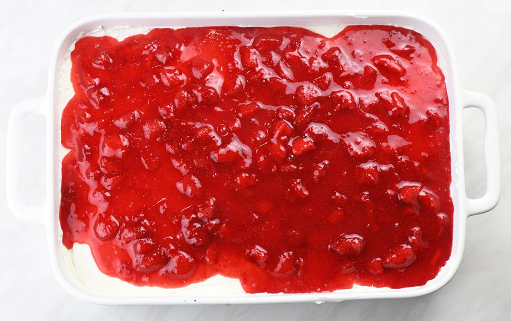 Strawberry filling on a cheesecake layer in a pan.