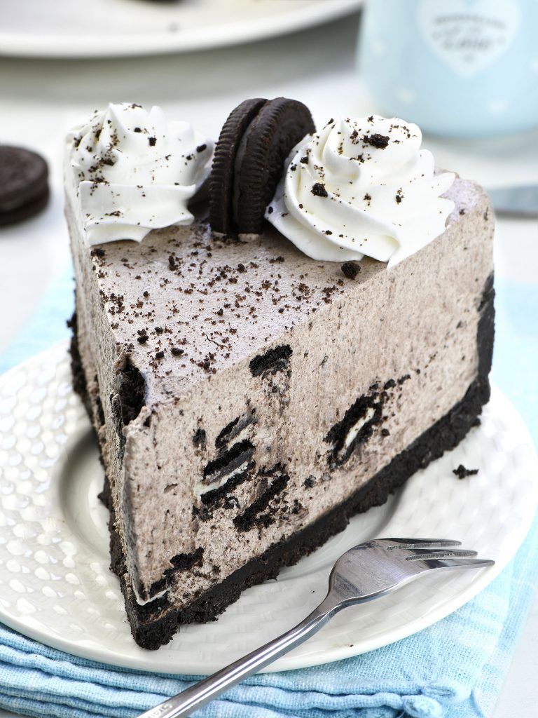 Close-up of No Bake Oreo Cheesecake slice with Oreo chunks and whipped cream topping.