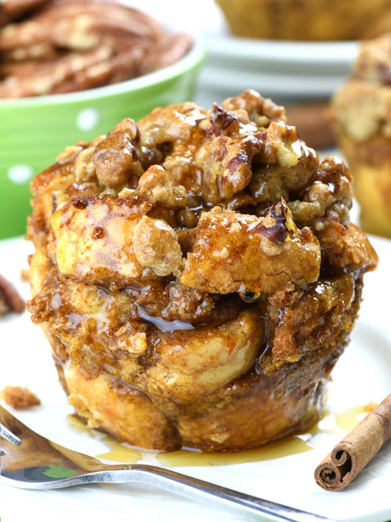 Close-up of a Pumpkin French Toast Muffin topped with a golden brown, crispy streusel and drizzled with syrup. The muffin is rich in cinnamon and pumpkin spices, creating a warm and inviting autumn treat. A cinnamon stick and fork sit beside the muffin, adding to the cozy dessert atmosphere.