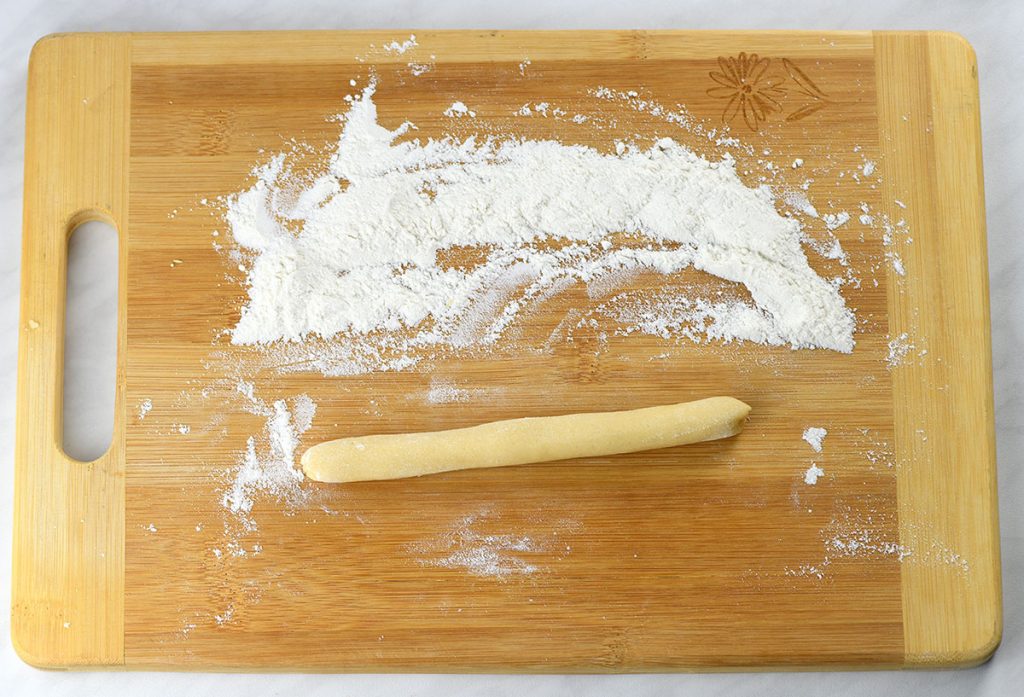 A floured wooden cutting board with a rolled log of Italian Christmas cookie dough. Flour is spread across the board, ready to prevent sticking as the dough is shaped.