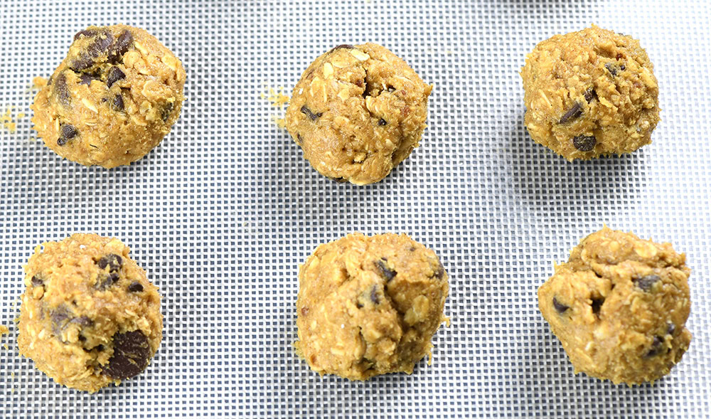 Raw oatmeal chocolate chip cookie dough balls arranged evenly on a baking mat, ready to be baked into delicious cookies.