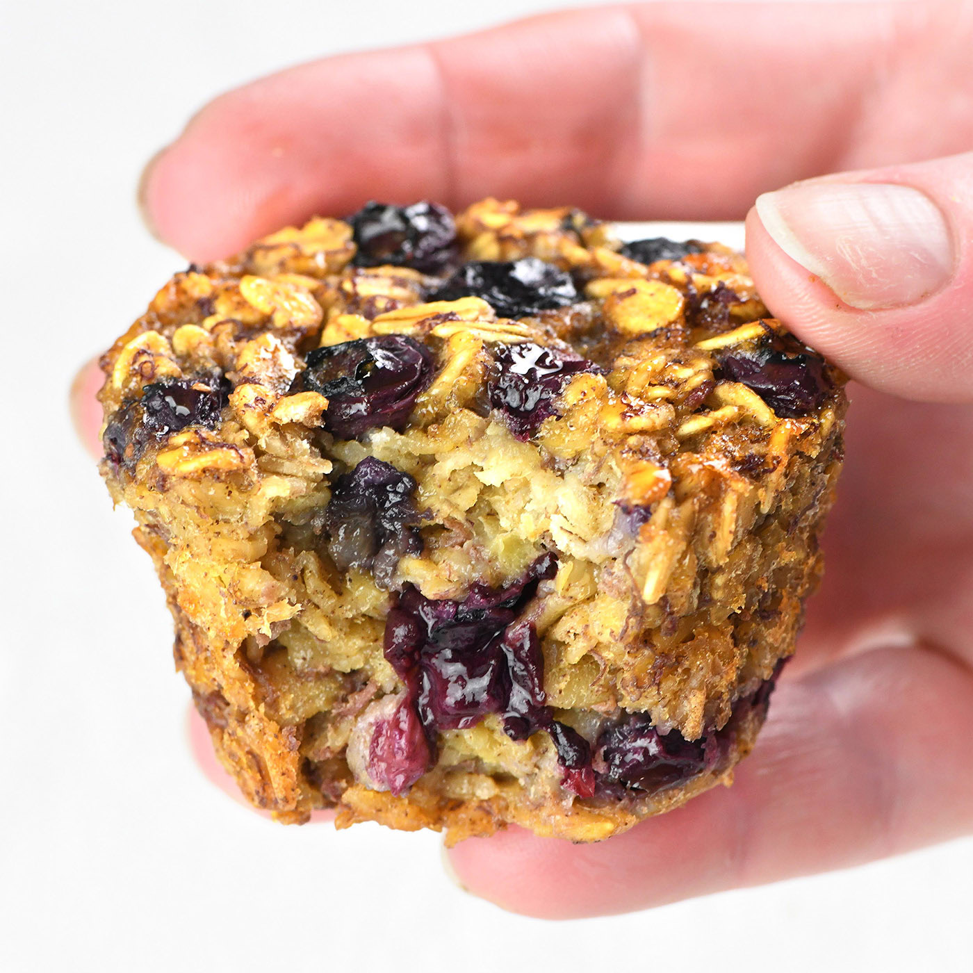 Hand holding a Blueberry Banana Baked Oatmeal Cup with a bite taken, showing the moist and fruity interior.