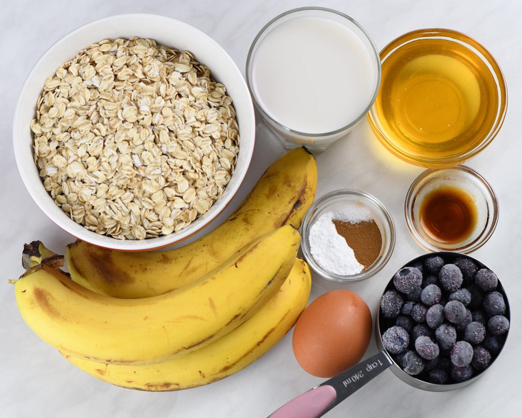 Ingredients for Blueberry Banana Baked Oatmeal Cups including oats, bananas, blueberries, honey, milk, egg, cinnamon, baking powder, and vanilla.
