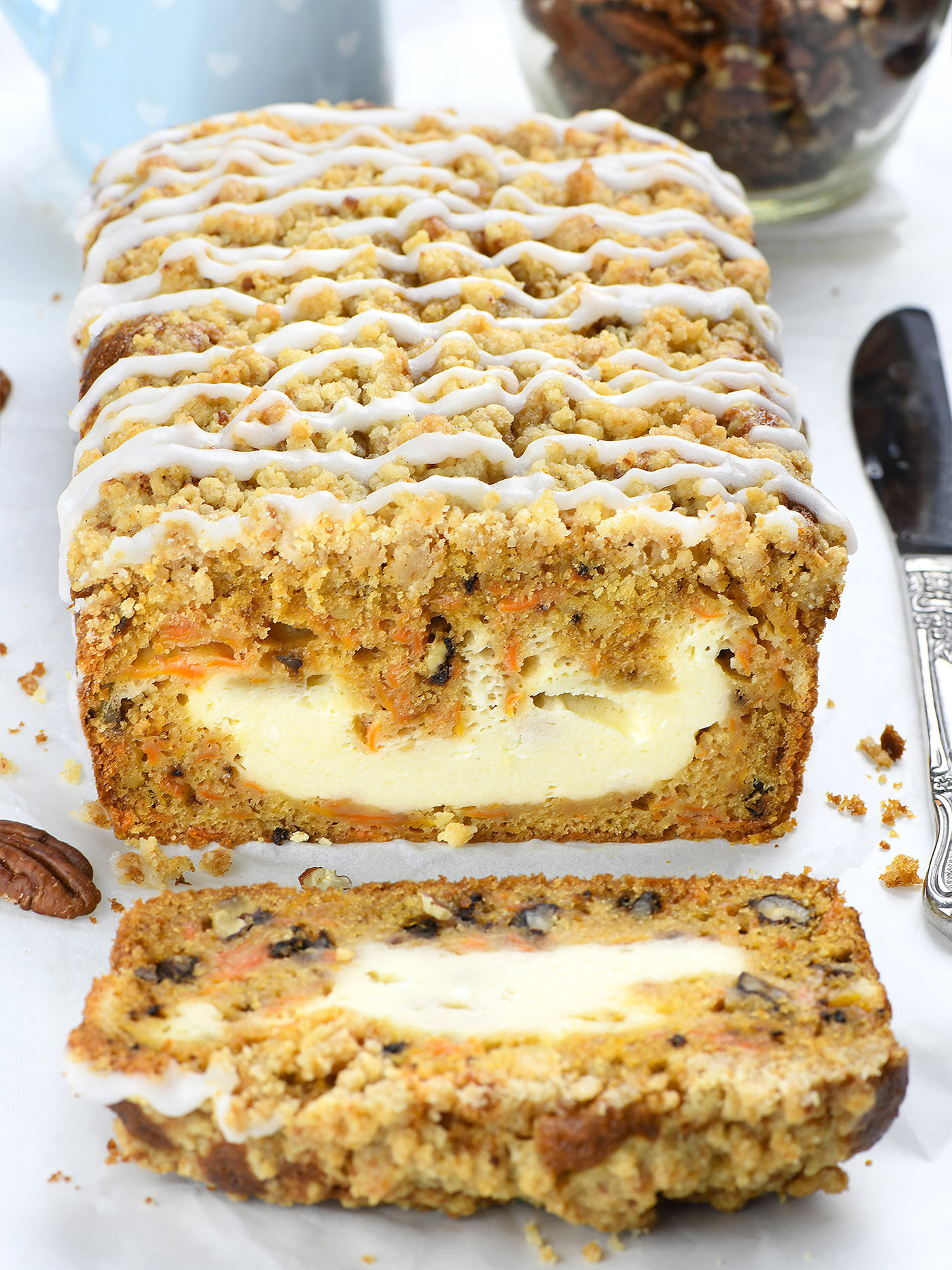 A freshly baked carrot cake loaf with a creamy cheesecake filling, topped with a crumbly streusel and drizzled with icing.