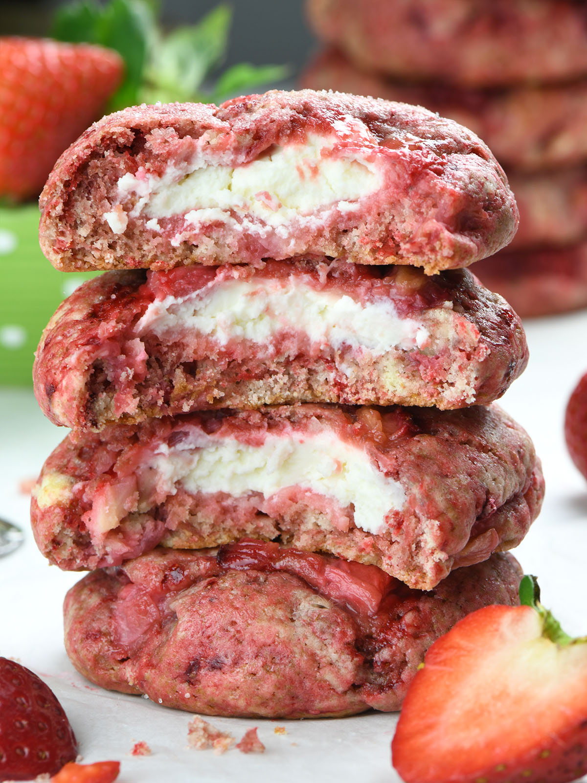 Close-up of strawberry cheesecake cookies stacked on top of each other, revealing a creamy cheesecake filling inside a soft, strawberry-infused cookie. Fresh strawberries are scattered around.