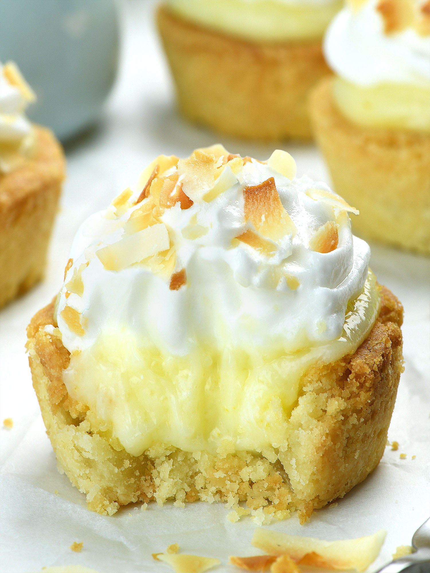 A Coconut Cream Pie Cookie Cup with a bite revealing the creamy coconut filling inside the soft cookie crust, topped with whipped cream and toasted coconut flakes.