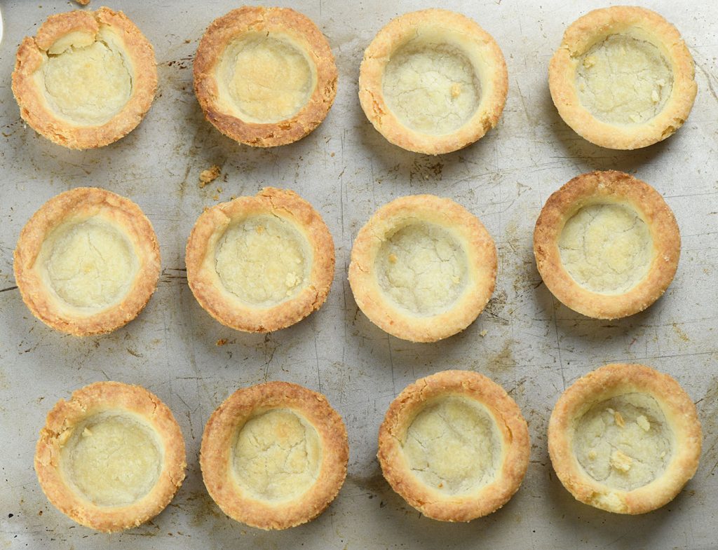 Freshly baked sugar cookie cups, golden and slightly cracked, cooling on a baking sheet, ready to be filled with creamy coconut pudding for the ultimate dessert.