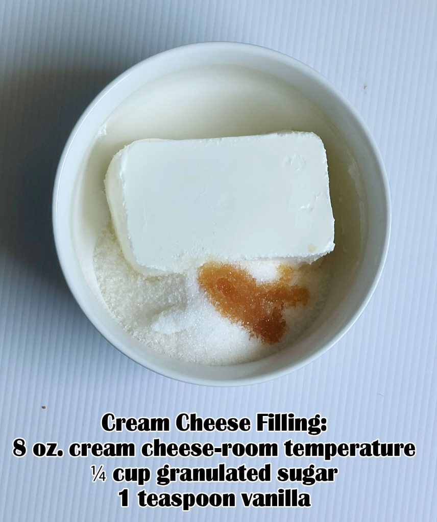 White bowl with cream cheese, granulated sugar, and vanilla extract on a white background — ingredients for a smooth cream cheese filling.