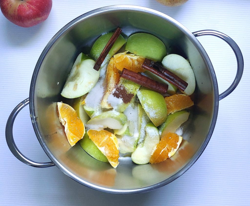 Pot filled with sliced apples, oranges, cinnamon sticks, cloves, and sugar – ingredients for making homemade apple cider.