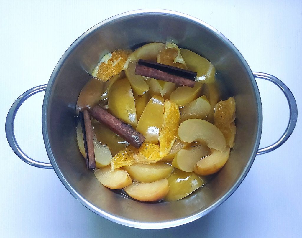 Apples, oranges, and cinnamon sticks simmering in a pot of water to make homemade apple cider.
